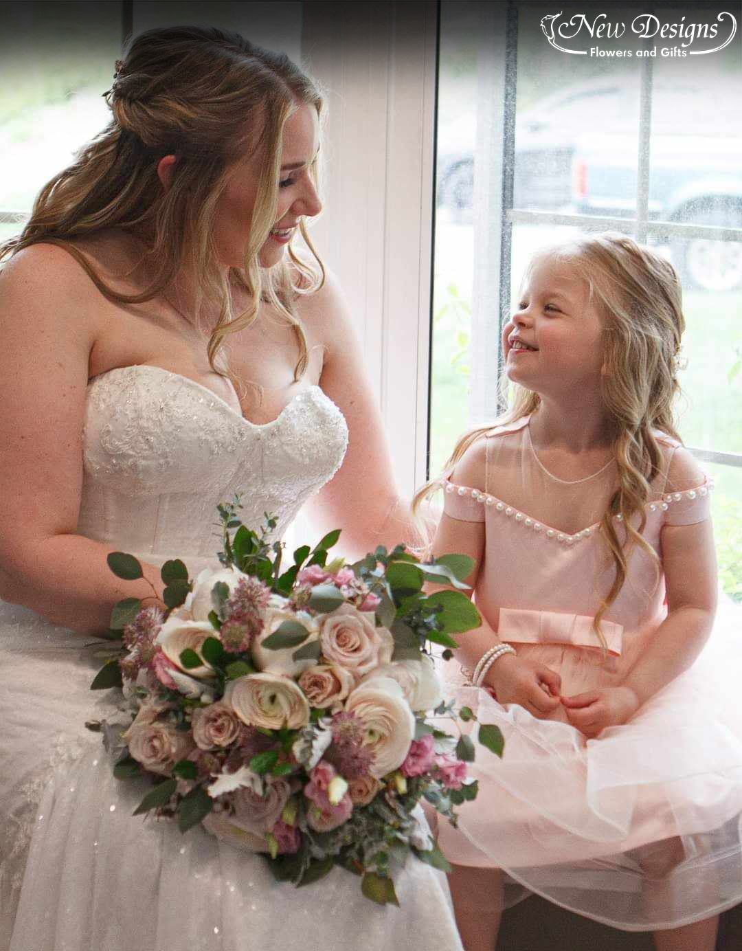 A bride sits with her flower girl holding a bouquet of Bright pinks and soft whites